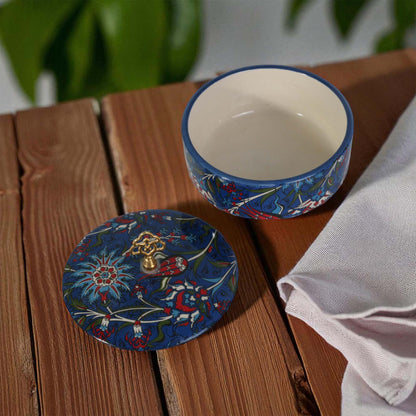 Decorative ceramic sugar bowl and lid on a wooden surface with a plant in the background