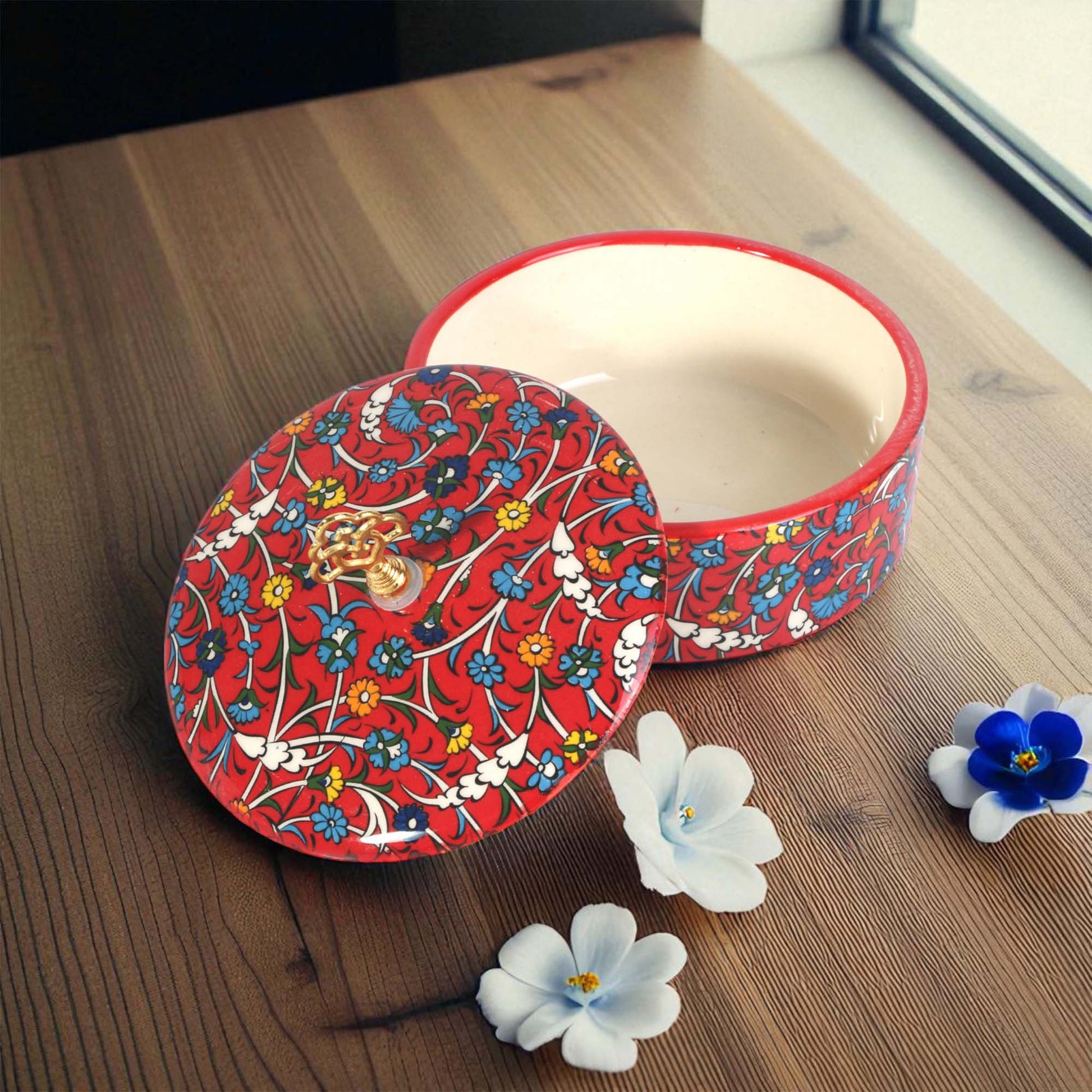Decorative red sugar bowl with floral patterns on a wooden surface with flowers.