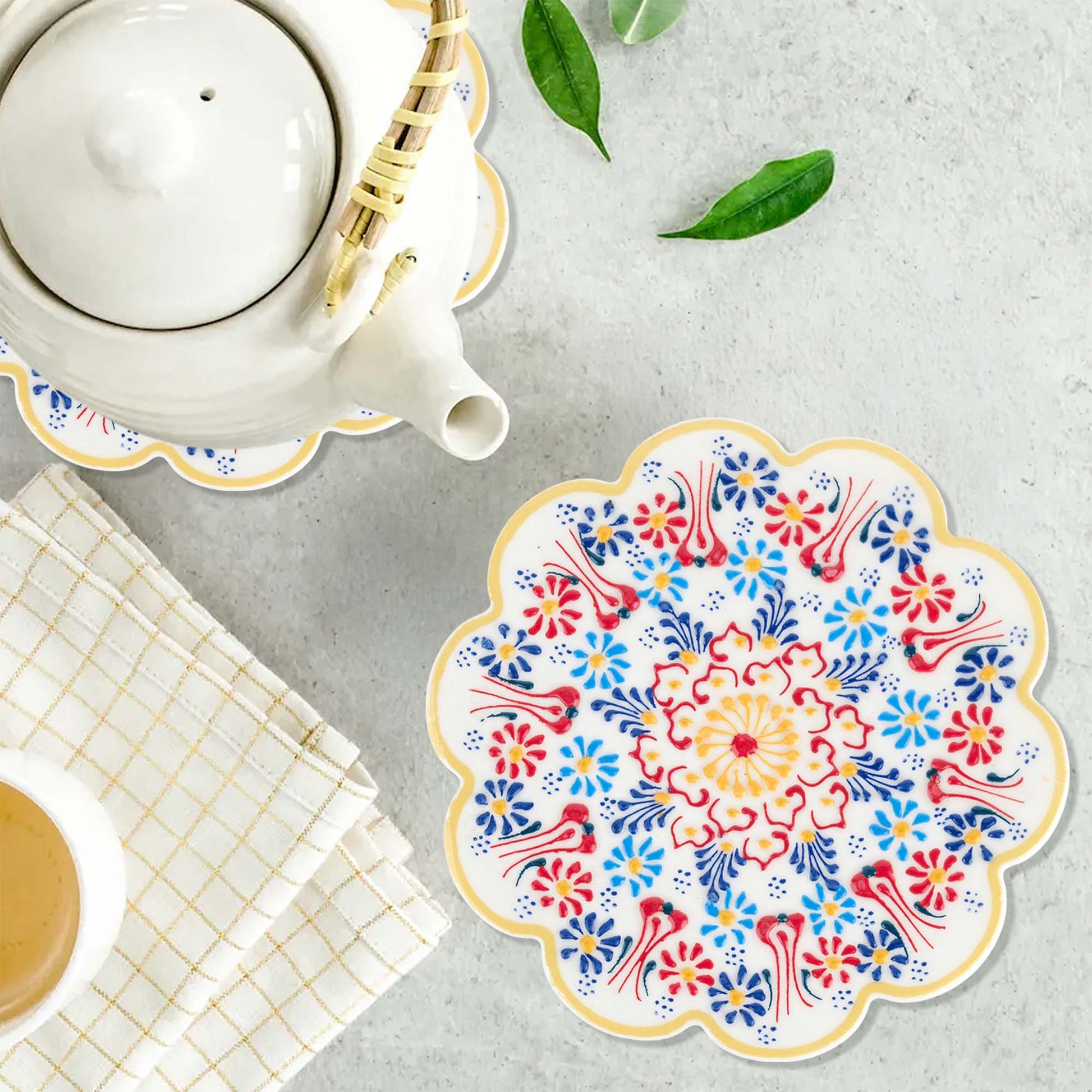 Decorative floral trivet on a table with a teapot and cup.