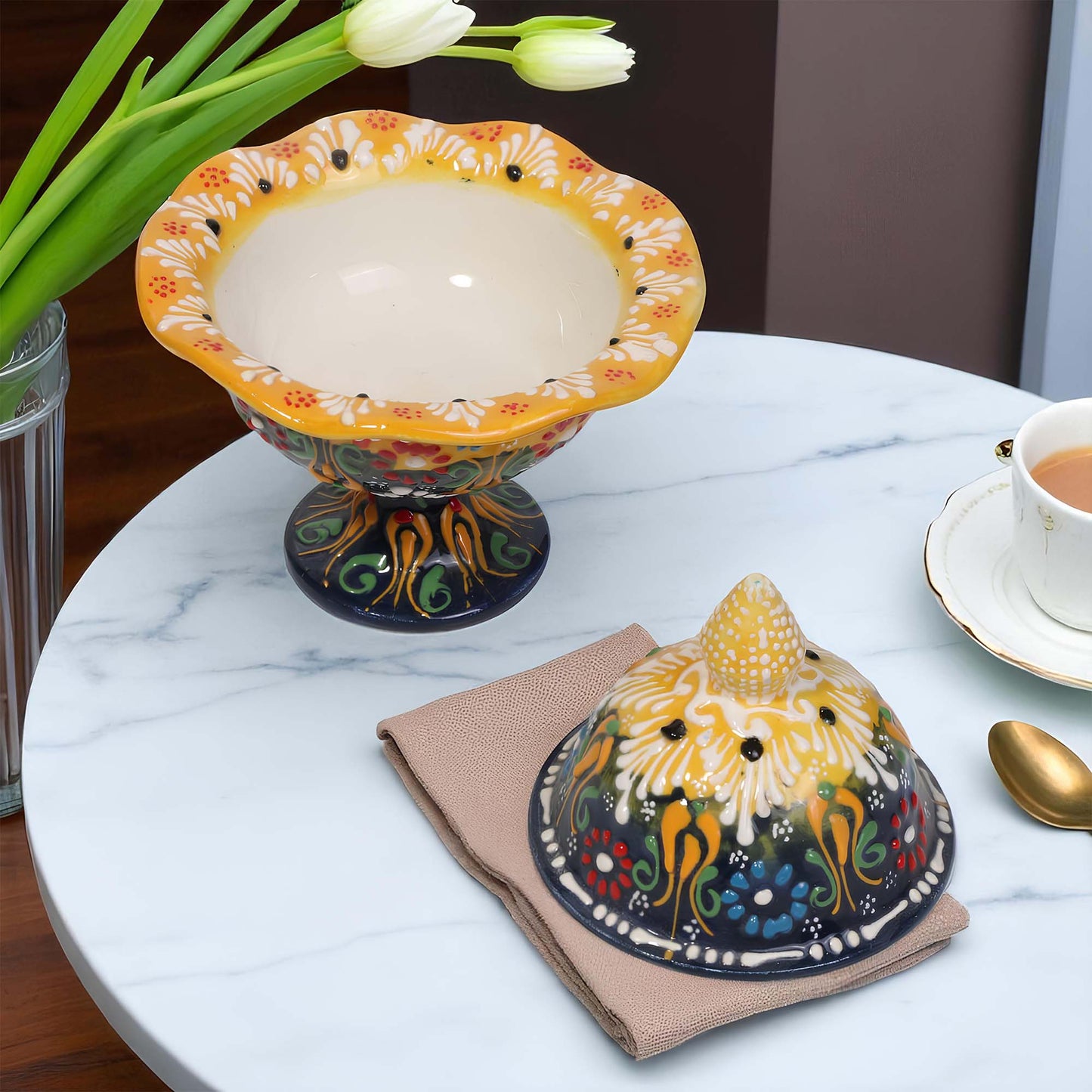 Decorative ceramic sugar bowl on a marble table with a cup of tea and flowers.