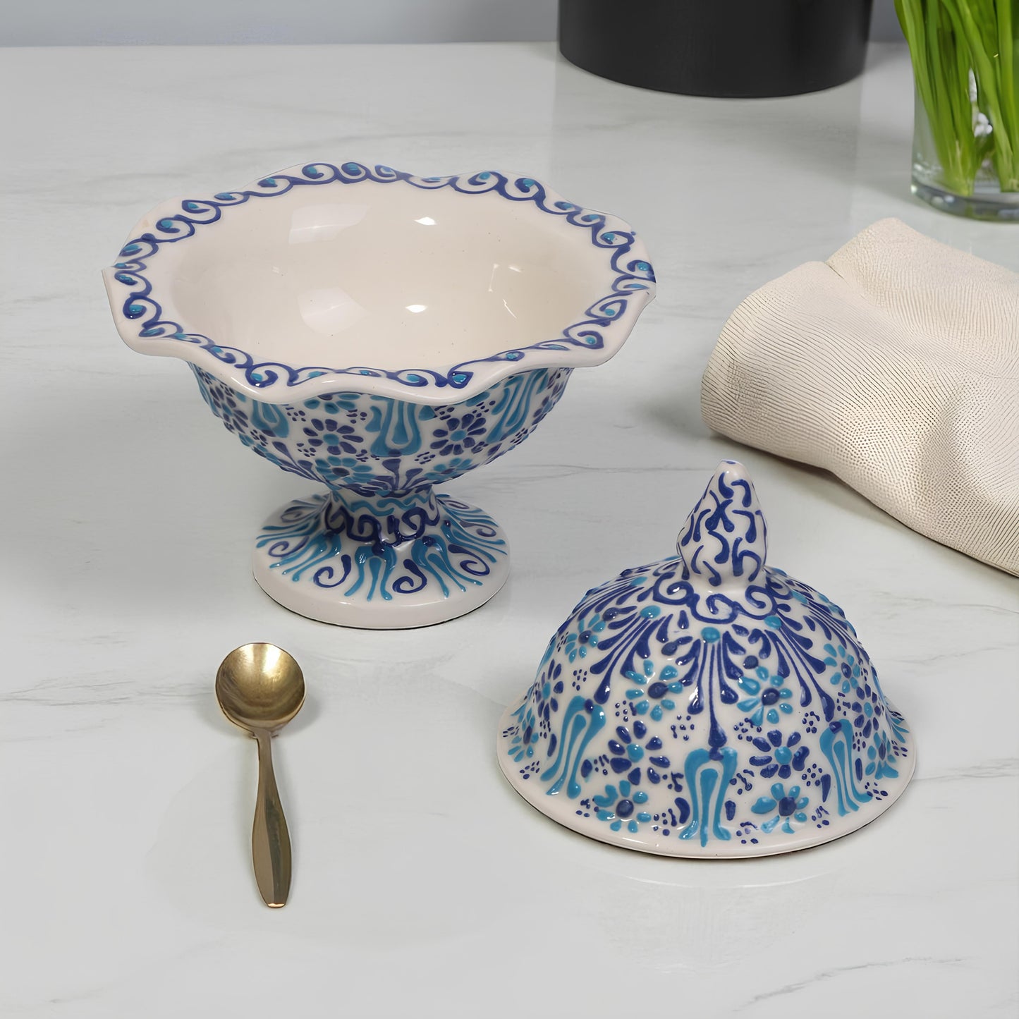 Decorative ceramic sugar bowl with blue patterns on a white surface with a spoon and a plant.