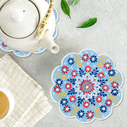 Decorative floral trivet on a table with a teapot and cup.